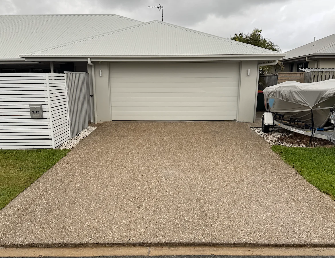Freshly cleaned exposed aggregate driveway in front of a white garage