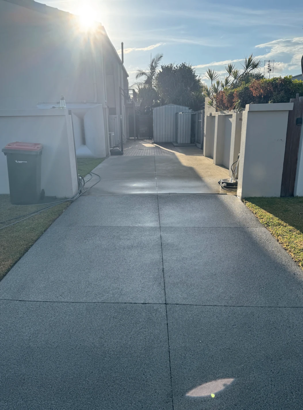 Freshly cleaned concrete driveway beside a home in afternoon sunlight